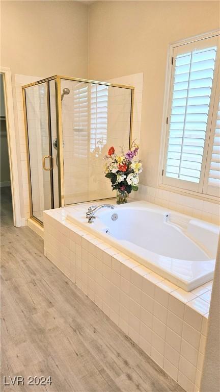 full bathroom featuring a stall shower, a garden tub, and wood finished floors