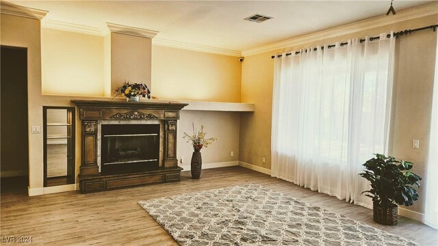 unfurnished living room featuring a large fireplace, baseboards, visible vents, ornamental molding, and wood finished floors