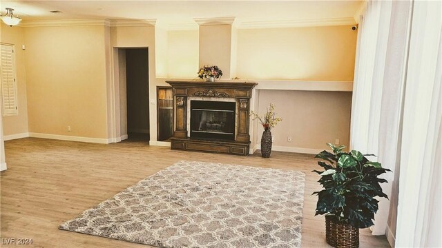 living room with ornamental molding, a glass covered fireplace, baseboards, and wood finished floors