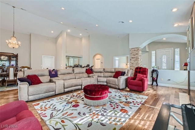 living room with high vaulted ceiling, light hardwood / wood-style flooring, an inviting chandelier, and ornate columns