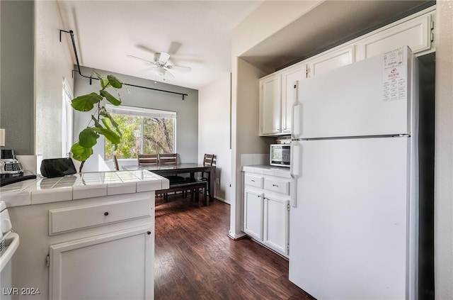 kitchen with tile countertops, white cabinetry, white fridge, dark wood-type flooring, and ceiling fan