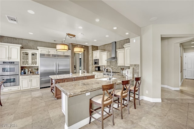 kitchen featuring light stone counters, a kitchen island, decorative light fixtures, wall chimney range hood, and stainless steel appliances