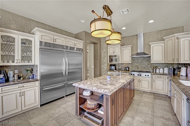 kitchen featuring light stone counters, sink, an island with sink, wall chimney exhaust hood, and stainless steel appliances