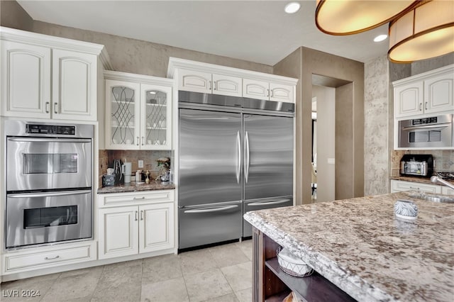 kitchen featuring light stone counters, sink, backsplash, white cabinetry, and stainless steel appliances