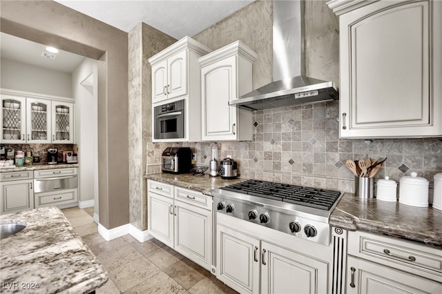 kitchen with tasteful backsplash, wall chimney exhaust hood, white cabinetry, stainless steel appliances, and dark stone counters