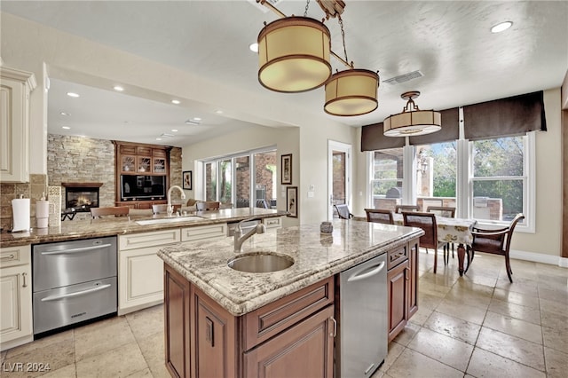 kitchen with light stone countertops, sink, pendant lighting, and an island with sink