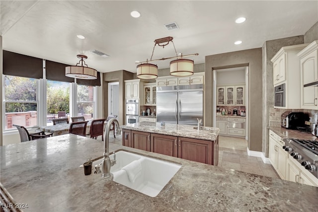 kitchen featuring appliances with stainless steel finishes, hanging light fixtures, a center island with sink, and sink