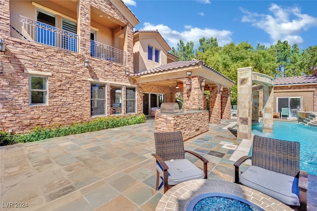 view of patio / terrace with a balcony, an outdoor kitchen, and pool water feature