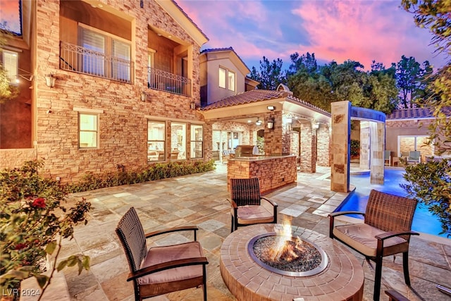 patio terrace at dusk featuring a balcony and a fire pit