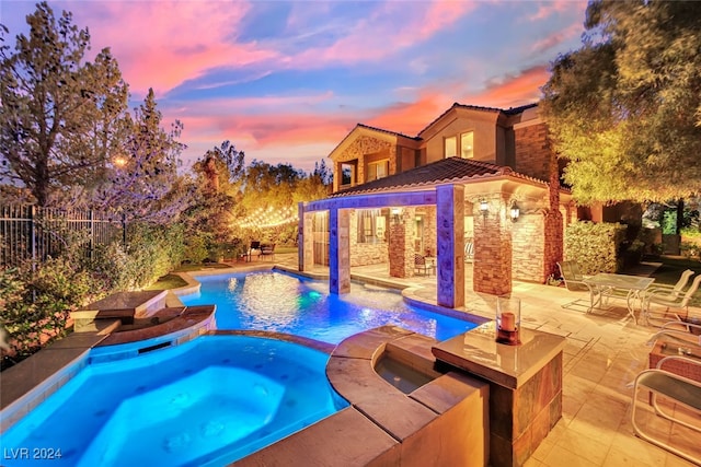 pool at dusk featuring an in ground hot tub and a patio area