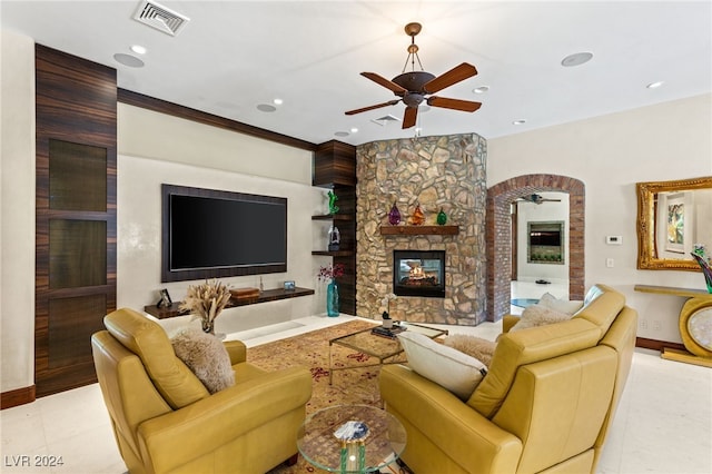 tiled living room featuring ceiling fan, ornamental molding, and a stone fireplace