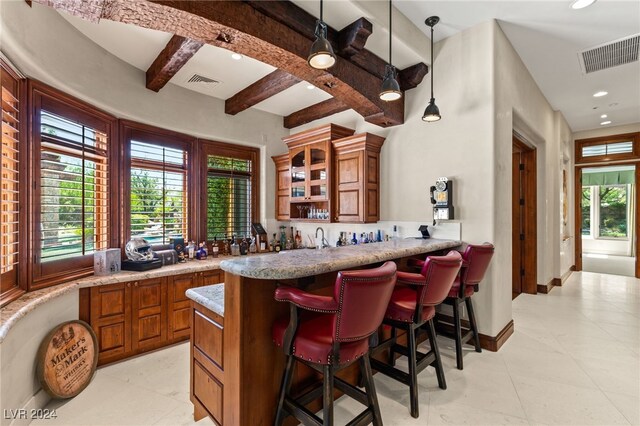 bar with light tile patterned floors, hanging light fixtures, light stone counters, and beamed ceiling