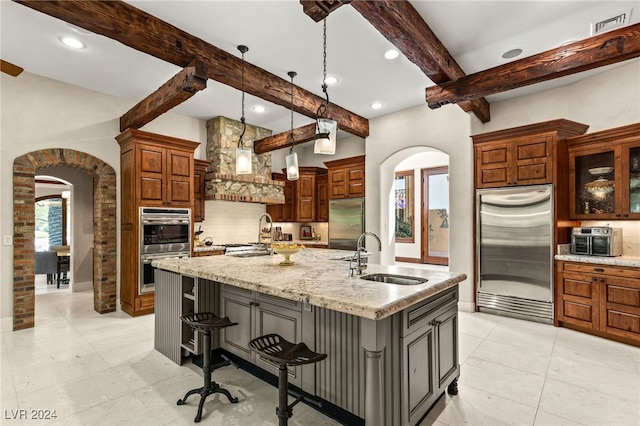 kitchen featuring an island with sink, light stone countertops, sink, appliances with stainless steel finishes, and a breakfast bar area