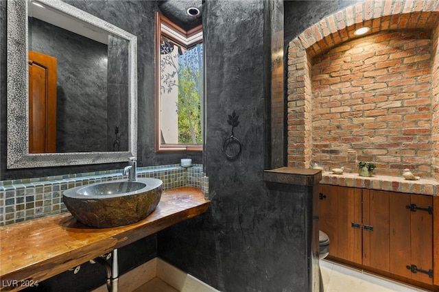 bathroom with brick wall, toilet, vanity, and tasteful backsplash