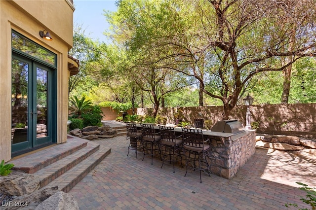 view of patio featuring grilling area, a bar, an outdoor kitchen, and french doors