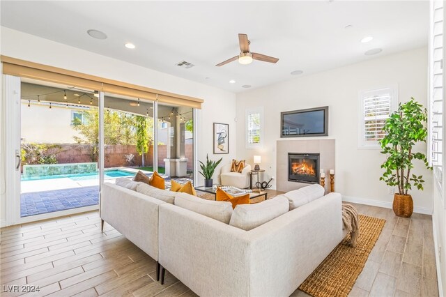 living room with ceiling fan, light wood-type flooring, and a tile fireplace