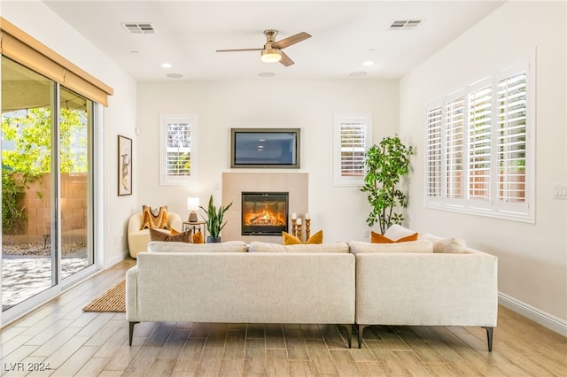 living room with light hardwood / wood-style flooring, a tile fireplace, plenty of natural light, and ceiling fan