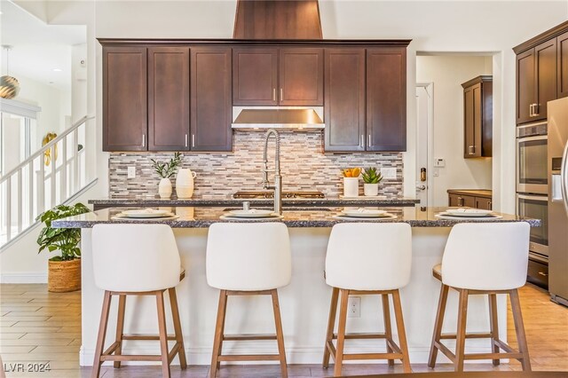 kitchen featuring light hardwood / wood-style flooring, dark stone counters, and an island with sink