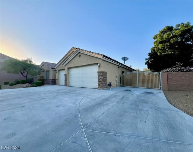 property exterior at dusk featuring a tiled roof, stucco siding, a gate, an attached garage, and concrete driveway