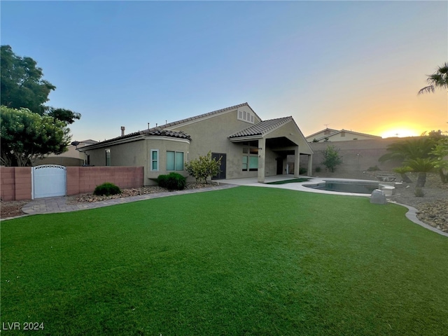 back house at dusk featuring a fenced in pool and a yard