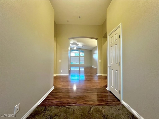 hallway featuring baseboards, arched walkways, wood finished floors, and lofted ceiling