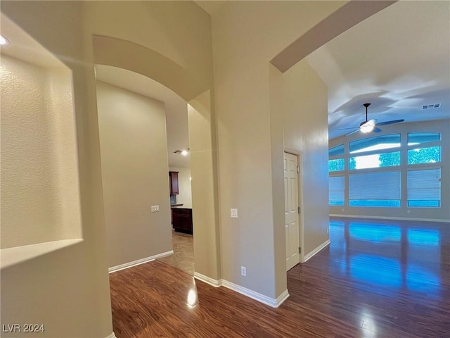 hall featuring arched walkways, wood finished floors, visible vents, and lofted ceiling