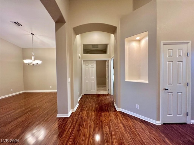 corridor with arched walkways, visible vents, baseboards, and wood finished floors