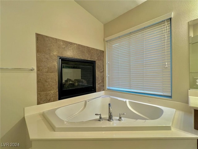 bathroom featuring a bath, a tile fireplace, and vaulted ceiling