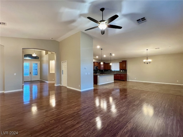 unfurnished living room with ceiling fan with notable chandelier, vaulted ceiling, sink, and dark wood-type flooring