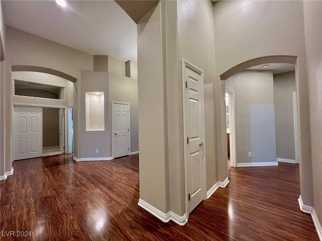 corridor featuring a high ceiling, arched walkways, wood finished floors, and baseboards
