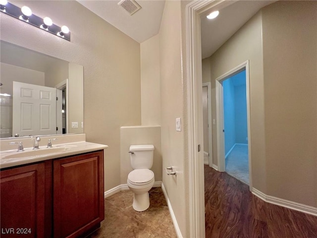 bathroom with toilet, vanity, baseboards, and visible vents