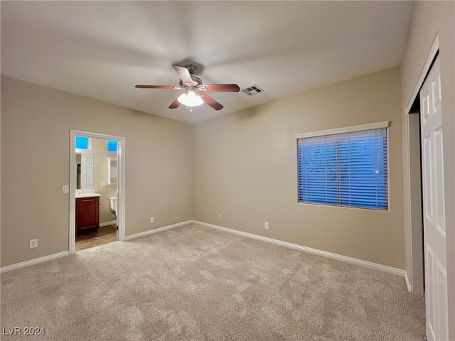 unfurnished bedroom with ceiling fan, ensuite bathroom, and light carpet