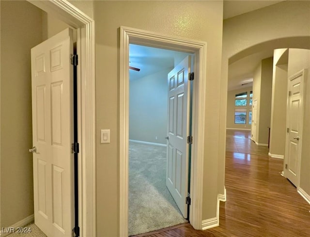 corridor featuring baseboards, arched walkways, and wood finished floors