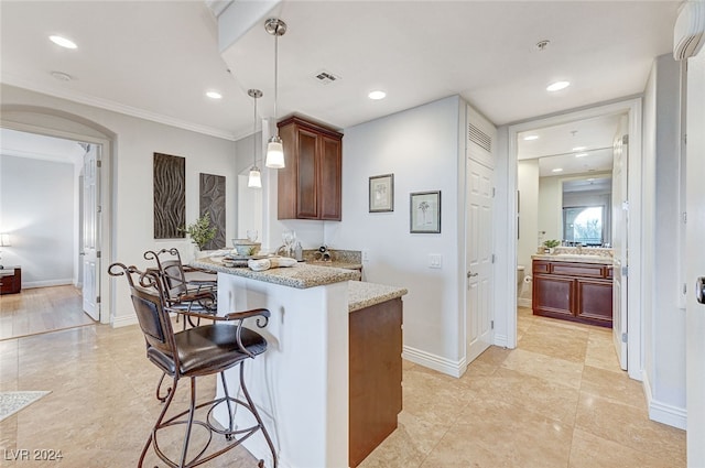 kitchen featuring pendant lighting, ornamental molding, light stone counters, kitchen peninsula, and a breakfast bar