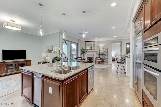 kitchen featuring ornamental molding, stainless steel appliances, sink, hanging light fixtures, and a center island with sink