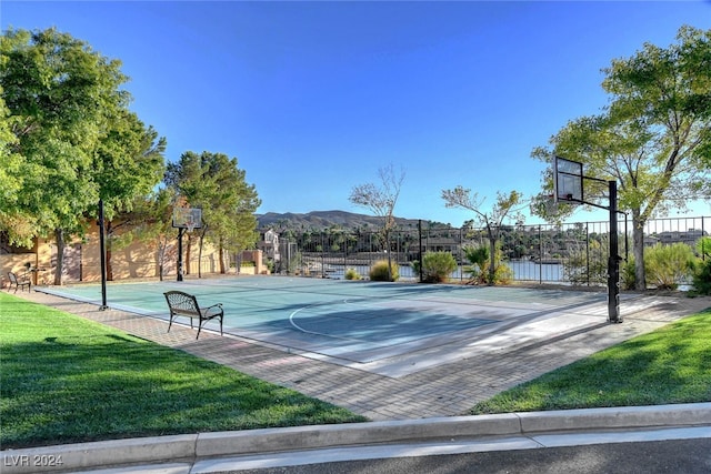 view of basketball court featuring a lawn, a mountain view, and a healthy amount of sunlight