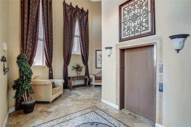entrance foyer featuring baseboards, stone tile flooring, and elevator