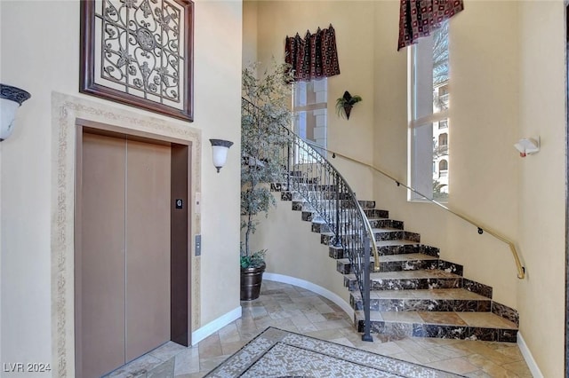 entrance foyer with baseboards, elevator, a towering ceiling, and stairs