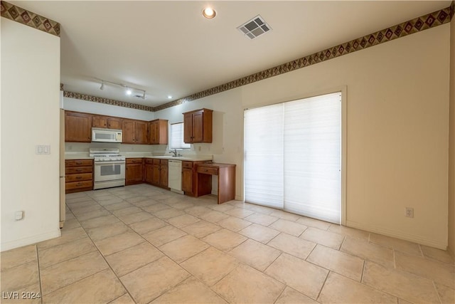 kitchen with white appliances, brown cabinetry, visible vents, baseboards, and light countertops