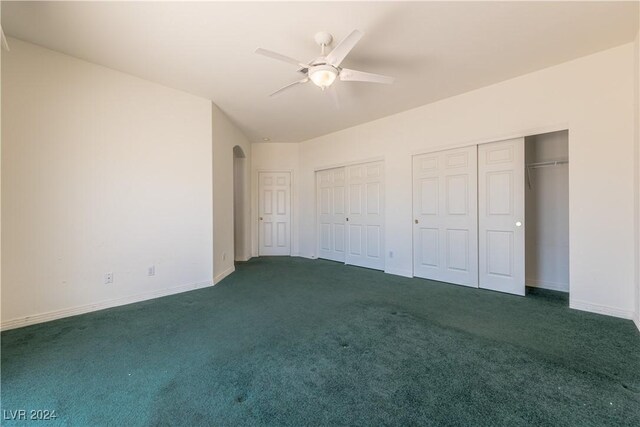 unfurnished bedroom with two closets, ceiling fan, and dark colored carpet