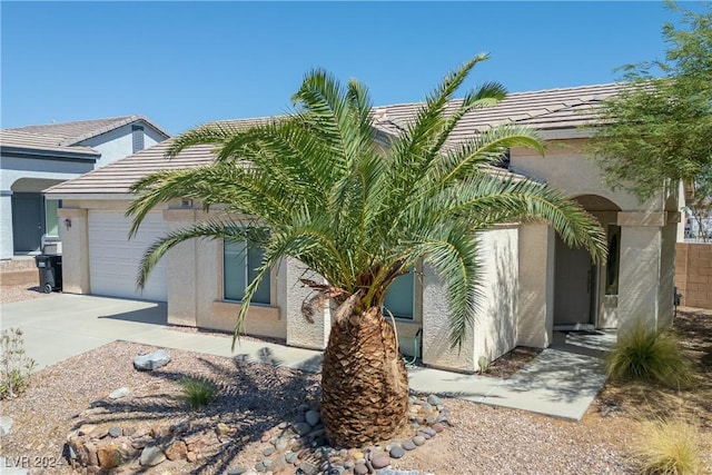 view of side of home featuring concrete driveway, a tiled roof, a garage, and stucco siding