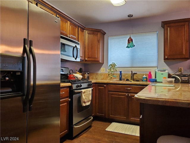 kitchen with sink, appliances with stainless steel finishes, dark hardwood / wood-style flooring, and decorative light fixtures