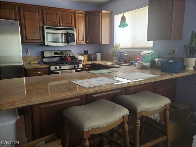 kitchen featuring light stone countertops, sink, hanging light fixtures, stainless steel appliances, and a breakfast bar area