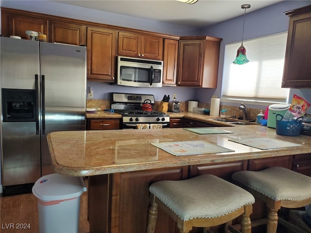 kitchen with appliances with stainless steel finishes, a breakfast bar area, sink, and pendant lighting