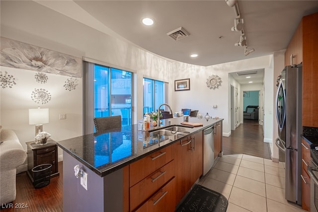 kitchen with dark stone countertops, stainless steel appliances, light hardwood / wood-style flooring, a center island with sink, and sink