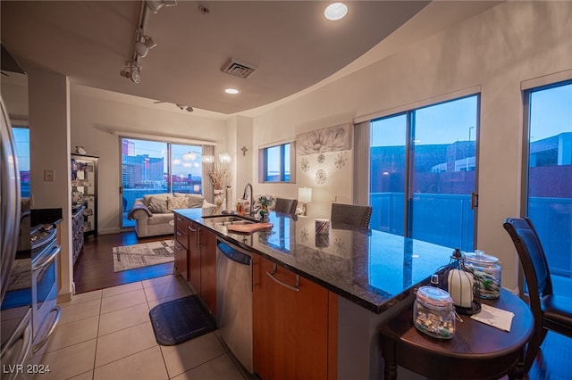 kitchen with light hardwood / wood-style floors, stainless steel appliances, a wealth of natural light, dark stone counters, and sink