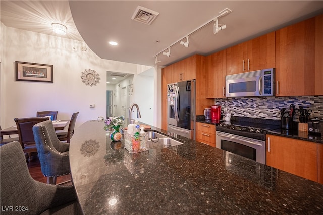 kitchen with sink, rail lighting, stainless steel appliances, a breakfast bar, and dark stone countertops