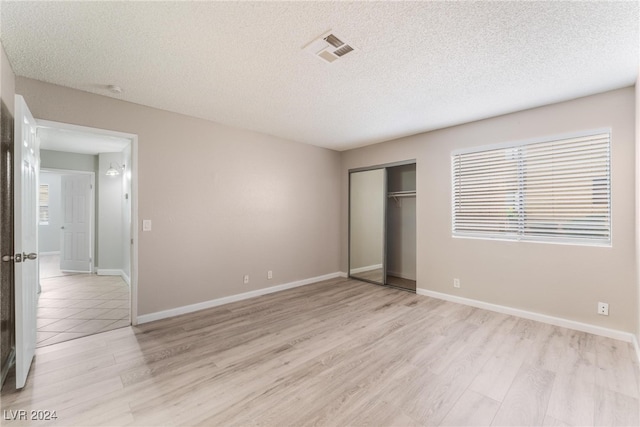 unfurnished bedroom with a closet, light hardwood / wood-style floors, and a textured ceiling