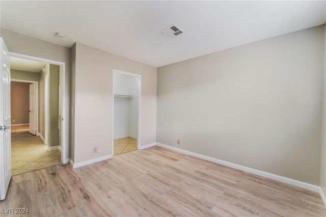 unfurnished bedroom with light hardwood / wood-style floors, a walk in closet, a textured ceiling, and a closet