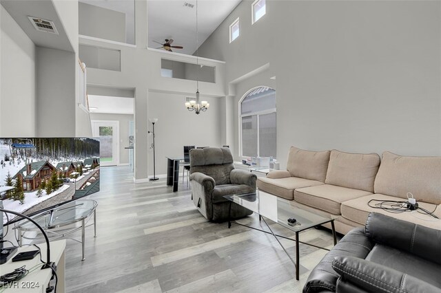 living room with ceiling fan with notable chandelier, light wood-type flooring, and a towering ceiling